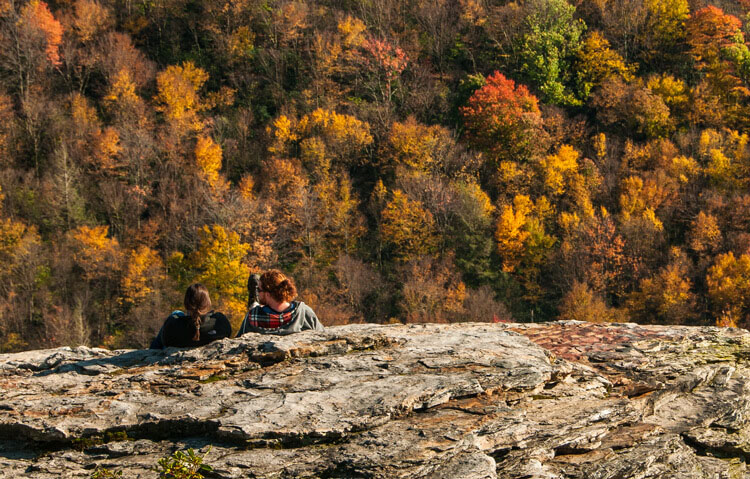 A couple sitting on a rock enjoying the Autumn view adds a romantic drama to the fall colors of the West Virginia Mountains