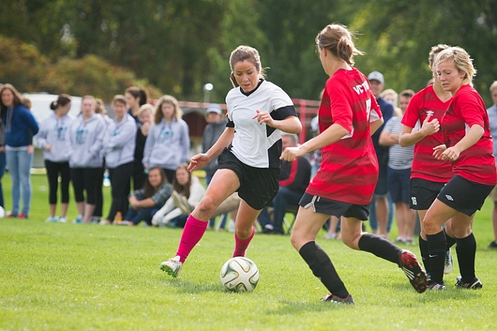 A female soccer player attempts to dribble the ball through two defenders
